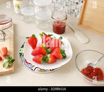 Zusammensetzung frischer Erdbeeren und leerer Gläser in der Küche. Saisonale Bauernprodukte und hausgemachte Konfitüren. Design-Hintergrund. Stockfoto