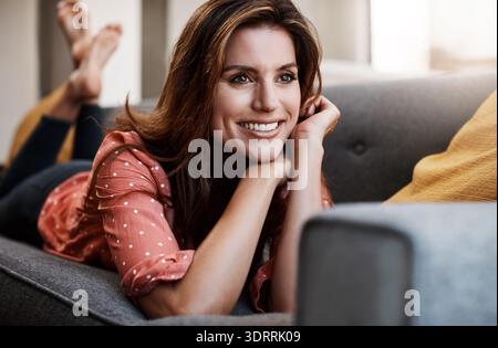 Zuhause, denkende und glückliche Frau auf der Couch zum Entspannen, Besinnung und Reflexion in der Lounge. Apartment, denken Sie daran und Person auf Sofa, Nostalgie und Ideen Stockfoto