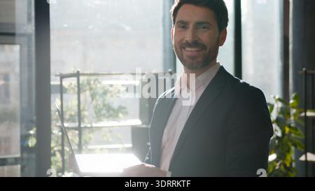 Erfolgreicher kaukasischer Geschäftsmann Tippen Laptop Morgenbüro lächelnd Kamera professioneller männlicher Leiter Manager arbeitet online selbstbewusster Chef Stockfoto