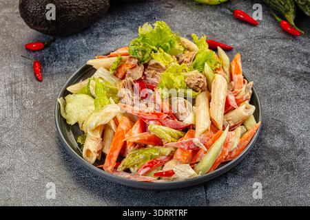 Appetitlicher Nudelsalat mit Thunfisch und Gemüse in einer cremigen Sauce. Die Top-Down-Ansicht auf dunklem Hintergrund hebt frische rote, grüne und beige Farben hervor. P Stockfoto