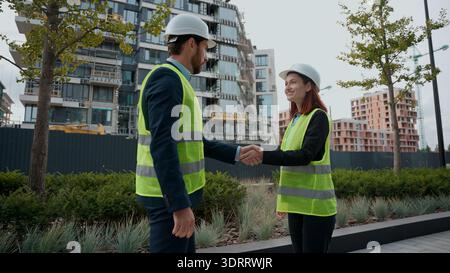Zwei Leute Ingenieure Mann Frau in Sicherheitsuniform Treffen Händeschütteln Kollegen in Helmen Hardhat Manager weibliche Führungskraft männlicher Arbeiter Stockfoto