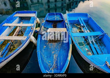 L’Ametlla de Mar, Spanien – drei blaue Holzfischboote, die in ruhigen Hafengewässern mit den nahe gelegenen Gebäuden vor Anker liegen Stockfoto
