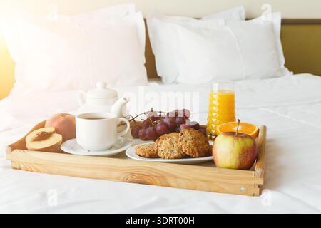 Köstliches Frühstückstablett auf einem Bett mit Obst und Getränken im Sonnenlicht Stockfoto
