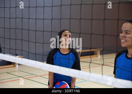 Verschiedene weibliche Teenager-Mannschaftskameraden in blauen Trikots halten Trikolore-Volleyball im Netz auf dem Fitnessplatz Stockfoto