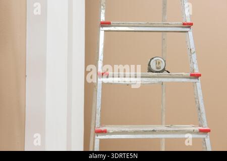 Stufenleiter und Maßband durch lackierte Wand im Zimmer oder Büro, das gerade renoviert wird. Werkzeuge für Reparatur- und Bauarbeiten Stockfoto