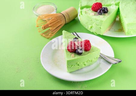 Leckerer grüner Matcha Käsekuchen ohne Backen, garniert mit frischen Heidelbeeren, Himbeeren, Mandel und Matcha Teepulver Streuseln. Köstliches süßes veganes Dessert, Stockfoto