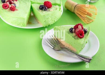 Leckerer grüner Matcha Käsekuchen ohne Backen, garniert mit frischen Heidelbeeren, Himbeeren, Mandel und Matcha Teepulver Streuseln. Köstliches süßes veganes Dessert, Stockfoto