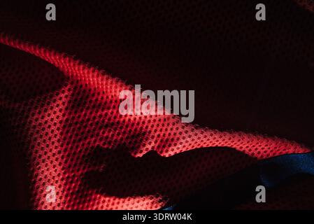 Rotes, technisches, sportliches Mesh-Gewebe mit Textur-Makro mit dramatischen Schatten und tiefen fließenden Falten für die Herstellung von Sportbekleidung und abstraktem Textil Stockfoto