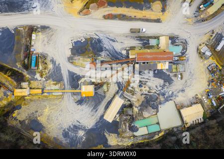 Aus der Vogelperspektive auf die raue Landschaft eines Steinbruchs, wo Erdtöne auf industrielle Strukturen unter einem riesigen Himmel treffen, Plouasne, Bretagne, Frankreich. Stockfoto