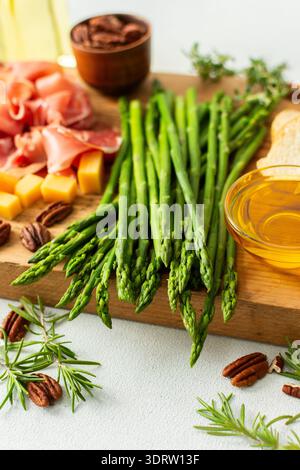 Verwöhnen Sie sich mit einer wunderschön gestalteten Wurstplatte mit lebhaftem Spargel, herzhaftem Wurstwaren, verschiedenen Käsesorten und frisch geröstetem Brot, ideal für Stockfoto