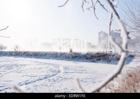 Zwei Personen gehen an einem nebeligen Wintermorgen auf einem schneebedeckten Pfad entlang, mit einer Skyline der Stadt in der nächtlichen Entfernung. Stockfoto