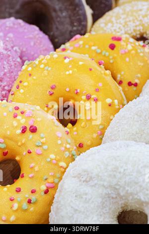 Eine ordentlich angeordnete Auswahl an Donuts mit glatten rosa, gelben und weißen Lasuren, die eine helle und appetitliche Präsentation schaffen. Nahaufnahme, Essen Stockfoto