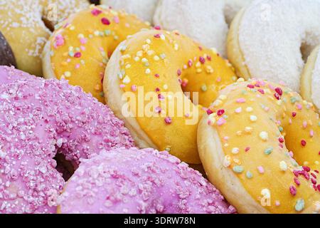 Eine ordentlich angeordnete Auswahl an Donuts mit glatten rosa, gelben und weißen Lasuren, die eine helle und appetitliche Präsentation schaffen. Nahaufnahme, Essen Stockfoto