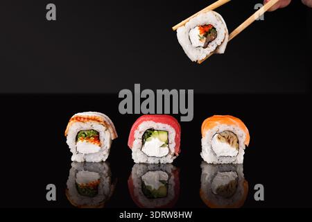 Sushi-Rolls sind in einem Set angeordnet und jemand hält eine Rolle mit Stäbchen Stockfoto