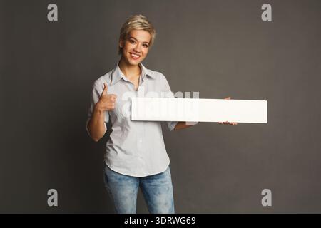 Junge Frau hält ein leeres Schild, während sie für eine Collage in einem Studio-Setting posiert Stockfoto