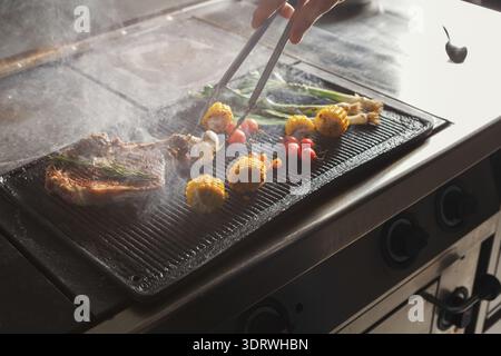 Die Hand reicht für gegrillte Speisen auf einer heißen Oberfläche in der Küche während des Kochens tagsüber Stockfoto