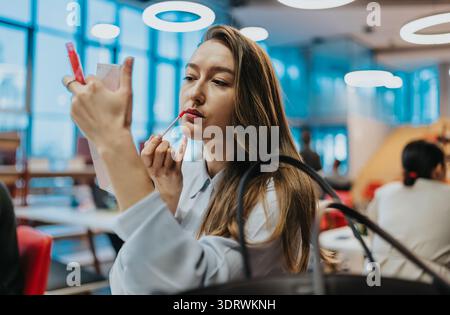 Frau trägt roten Lippenstift in einem hellen, modernen Café-Ambiente und blickt in einen Spiegel Stockfoto