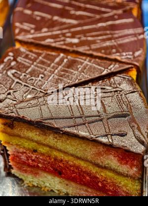 Mehrschichtiges Schwammkuchen-Foto mit Schokoladenglasur-Topping und bunten Kuchen-Schichten Nahaufnahme vertikaler Hintergrund. Stockfoto