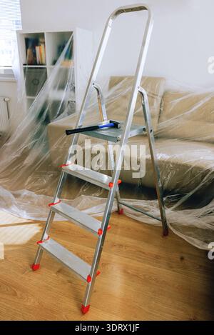 Aluminium-Stufenleiter mit Hammer in einem Wohnzimmer, das während der Renovierung des Hauses mit Kunststoff bedeckt ist Stockfoto
