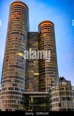 2026 Paris. Moderne Glastürme mit goldenen Lichtern vor einem tiefblauen Abendhimmel, die elegante architektonische Kurven und urbane Eleganz zeigen. Stockfoto