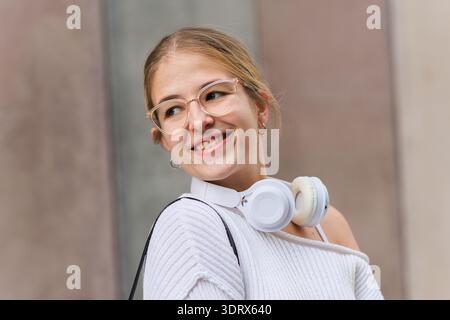 Junge Studentin lächelt mit Kopfhörern auf dem Campus Stockfoto