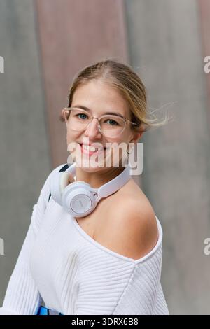 Junge Studentin lächelt mit Kopfhörern auf dem Campus Stockfoto