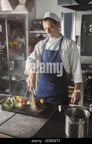 Ein Koch kocht Fleisch, während er Zangen verwendet Stockfoto