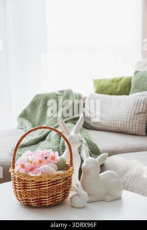 Osterkorb mit Ester-Eiern, Plüschhase und Frühlingsdekor auf weißem Tisch im Cozy Wohnzimmer Stockfoto