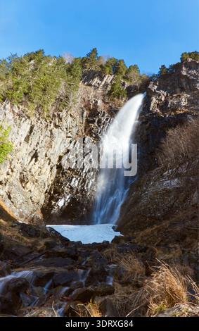 Majestätischer Wasserfall, der die Basalt Cliffs unter klarem blauem Himmel Hinunterstürzt. Eine atemberaubende Langzeitaufnahme eines hohen Wasserfalls, der über ein einzigartiges Felsformat fließt Stockfoto