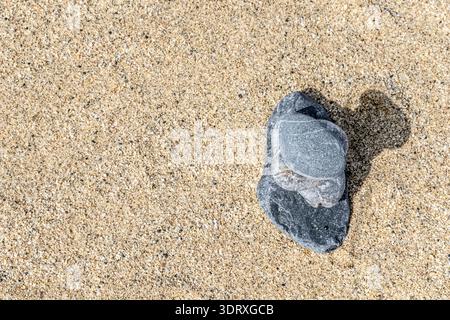 Draufsicht auf einen ausgeglichenen Kieselstein an einem Sandstrand mit großem Kopierraum für Text. Eine minimalistische Komposition im Zen-Stil, die Harmonie und Stabilität symbolisiert Stockfoto