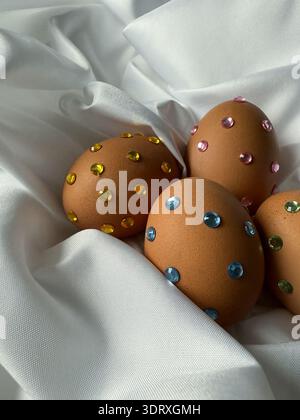 Ostereier mit Glitzersteinchen auf weißem Seidenstoff. Osterfeierstraditionen, Designideen für Kinder. Stockfoto