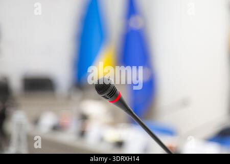 Konferenzmikrofon mit ukrainischen und europäischen Flaggen im Hintergrund als Symbol für internationale Verhandlungen. Stockfoto