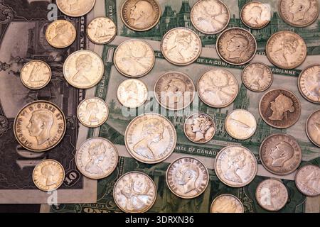 Gemischte Münzen in den Kanadischen, USA und Bahama-Inseln, Silber 5, 10, 25, 50 Cent auf dem Hintergrund alter kanadischer Papierwährungsscheine. Stockfoto