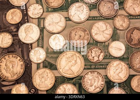 Gemischte Münzen in den Kanadischen, USA und Bahama-Inseln, Silber 5, 10, 25, 50 Cent auf dem Hintergrund alter kanadischer Papierwährungsscheine. Stockfoto