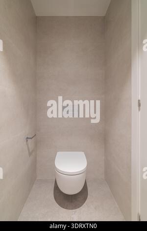 Ein modernes, minimalistisches Badezimmer mit einer weißen Toilette vor einer hellgrauen gefliesten Wand. Der Raum ist sauber und übersichtlich, was die Einfachheit betont. Stockfoto