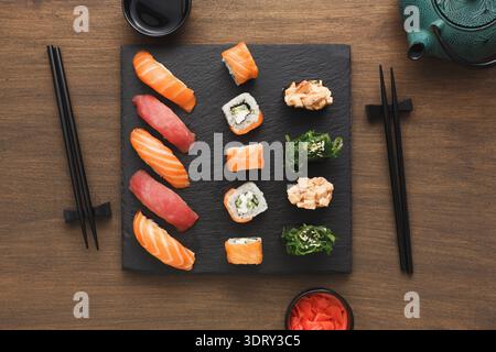 Verschiedene Sushi-Sorten serviert auf einem schwarzen Teller mit Stäbchen und grünem Tee Stockfoto
