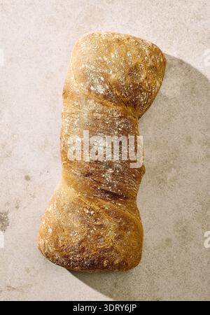 Blick von oben auf ein rustikales handwerkliches Brotbrot Ciabatta mit knuspriger Kruste auf einem hellen strukturierten Hintergrund. Natürliche Zusammensetzung von Backwaren geeignet für Stockfoto