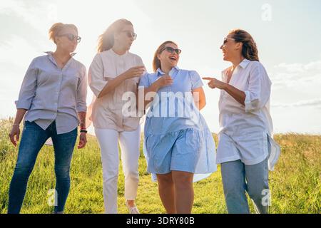 Fröhliche, abwechslungsreiche Frauen, die Hand in Hand halten, gehen durch grüne Wiesen, um Freundschaft und Glücksgefühle mit vier schönen fr. zu genießen Stockfoto