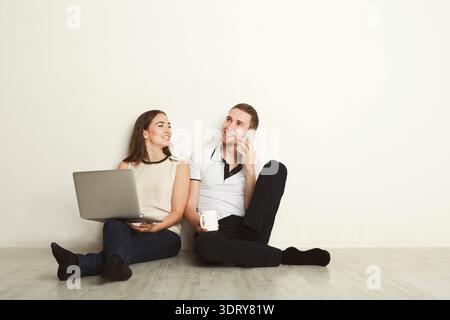Ein Paar sitzt auf dem Boden und arbeitet an einem Laptop und genießt gemeinsam Kaffee Stockfoto