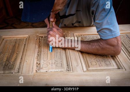 Ein Nahaufnahme, in dem das Können eines marokkanischen Handwerkers festgehalten wird, während er komplexe geometrische Details auf eine Holzplatte schneidet. Das Bild hebt die Exp Stockfoto