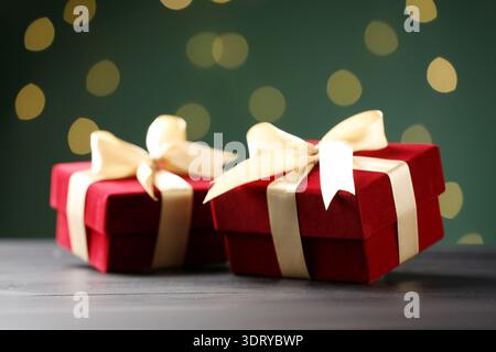 Schöne Samtgeschenkdosen auf schwarzem Holztisch vor dunkelgrünem Hintergrund mit verschwommenen Lichtern, Nahaufnahme. Bokeh-Effekt Stockfoto