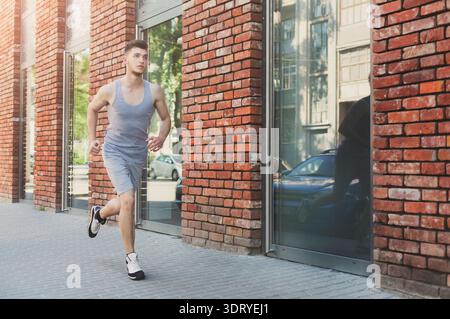 Ein junger Mann läuft am Morgen in einer Stadt an einem Backsteinhaus entlang Stockfoto