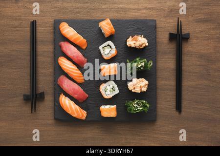 Sushi auf einem schwarzen Schieferteller auf einem Holztisch mit Stäbchen daneben angeordnet Stockfoto