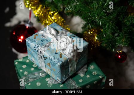 Nahaufnahme der Weihnachtsszene mit zwei Geschenkboxen, die unter einem Weihnachtsbaum gestapelt sind. Das obere Präsent ist in blau gemustertes Papier gewickelt und mit einer Wide gebunden Stockfoto