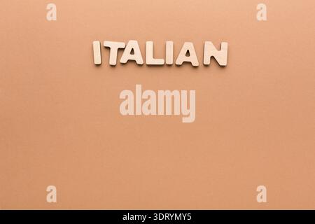 Das Wort „Italienisch“ besteht aus hellen Holzbuchstaben auf einem unkomplizierten Hintergrund Stockfoto