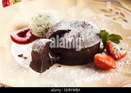 Köstliches Schokoladendessert mit Melting Center serviert mit Eis und Erdbeeren auf einem Teller Stockfoto
