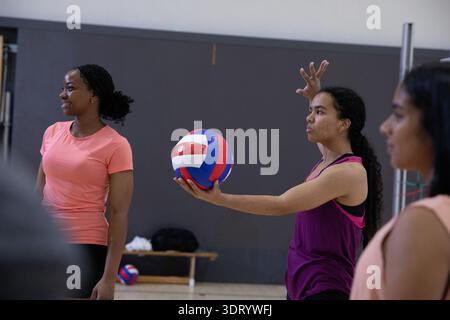 Verschiedene weibliche Teenager im Fitnessstudio, Kellner in lila Tank mit rot-weiß-blauem Ball, Kopierraum Stockfoto