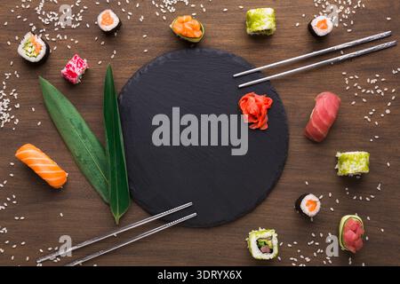 Collage aus Sushi-Stücken, die um eine Schieferplatte mit Stäbchen auf einem Holztisch angeordnet sind Stockfoto