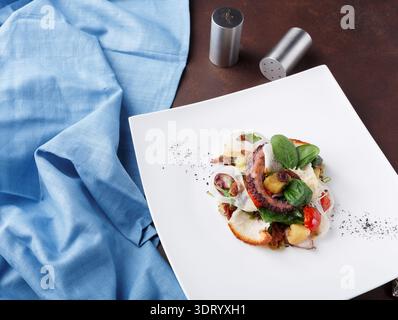 Frischer Oktopussalat serviert auf elegantem Teller mit blauem Tuch im Hintergrund für ein kulinarisches Erlebnis Stockfoto