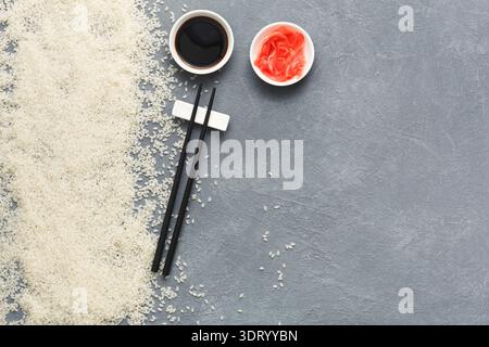 Reis, Sojasauce, Ingwer und Essstäbchen befinden sich auf einer grauen Oberfläche in einem einfachen Setup für das Essen Stockfoto
